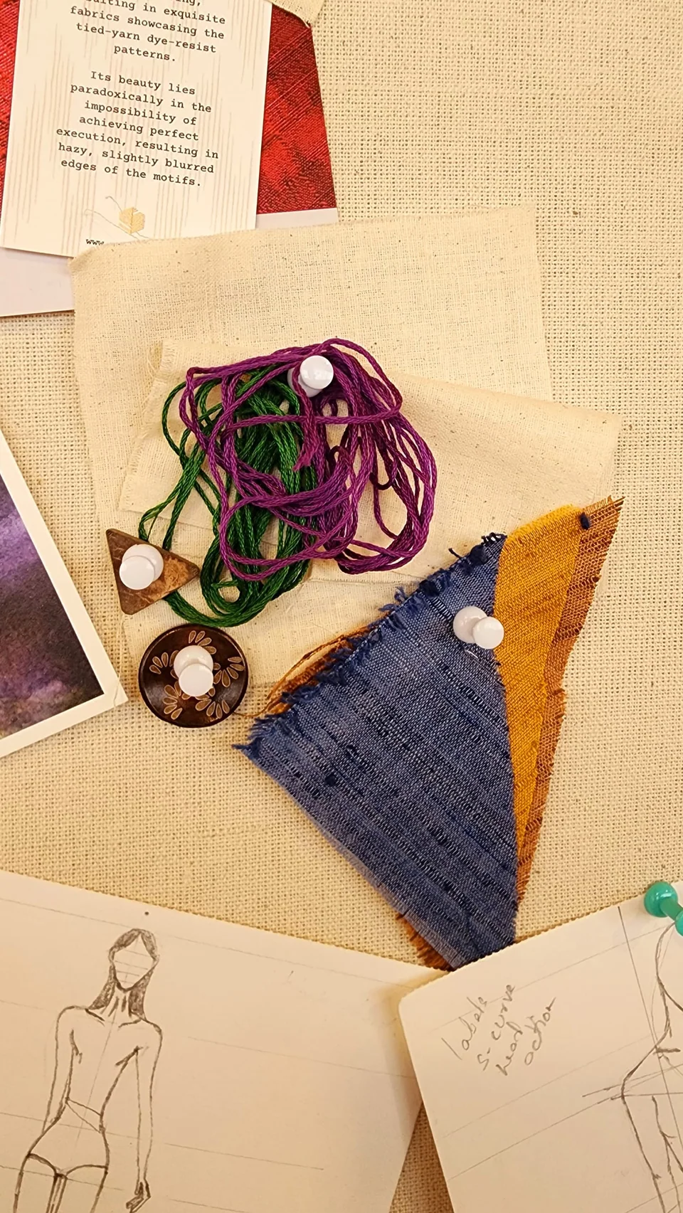 Design sketches on paper with fabric swatches and skeins of thread laid over them