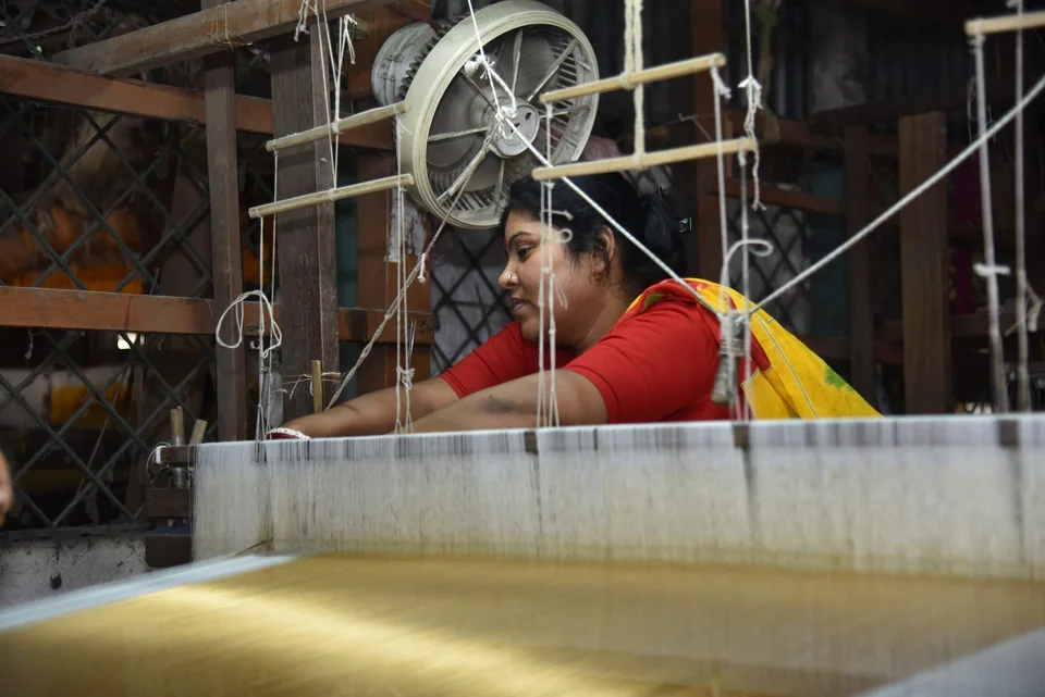 A weaver at her home loom in Fulia with yellow silk on the warp